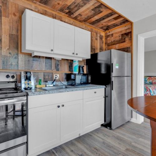 A kitchen with white cabinets, stainless steel appliances, wood accents, and a round wooden table. Doorway leads to another room.