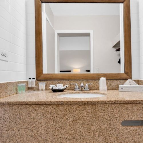 The image shows a bathroom vanity with a large mirror, toiletries, a sink, and a tissue box on a granite countertop.