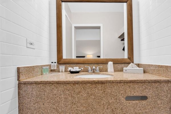 A bathroom sink with a granite countertop, toiletries, a wooden mirror, and white tiled walls.