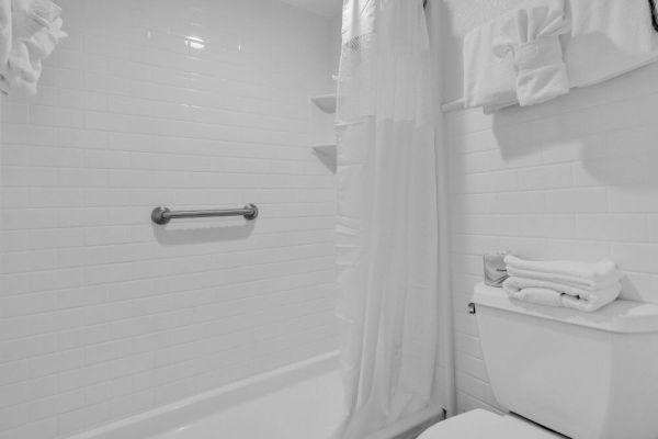 The image shows a white-tiled bathroom with a shower, curtain, towel rail, and toilet with neatly folded towels on top.