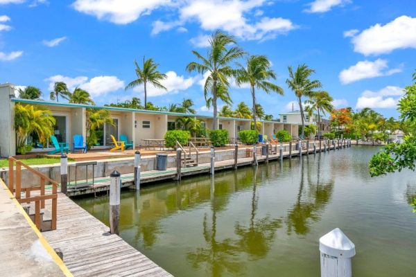 A scenic waterfront view with tropical-style houses, palm trees, and a clear blue sky reflected in the calm waterway.