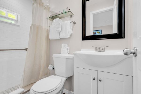 A clean bathroom with a shower, toilet, white vanity, mirror, and towels neatly arranged on a rack above the toilet.