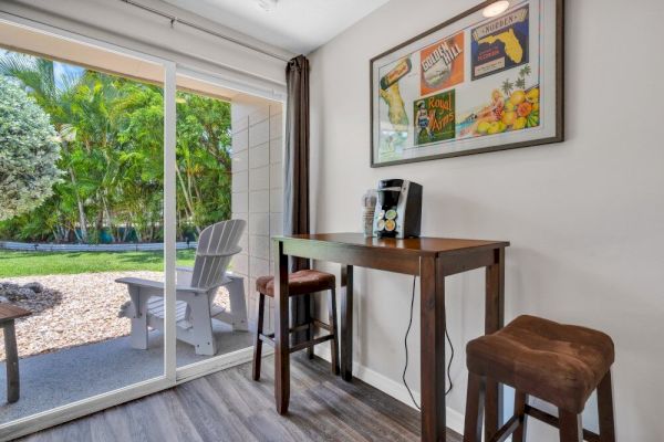 A small indoor table with stools, a coffee maker, and wall art is next to a sliding glass door leading to an outdoor patio area.