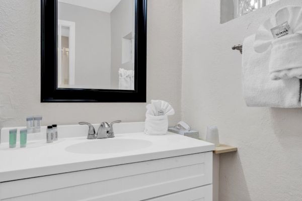 A clean bathroom with a white vanity, a mirror, towels, and toiletries neatly arranged on the countertop and a towel rack.