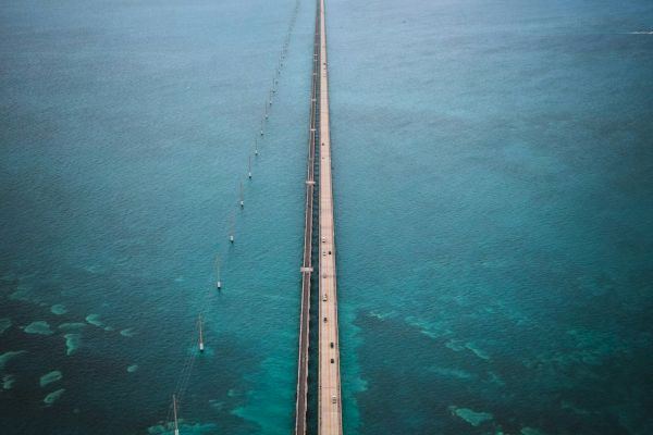 A long bridge stretches across turquoise waters towards a distant island, under a cloudy sky, creating a scenic view.