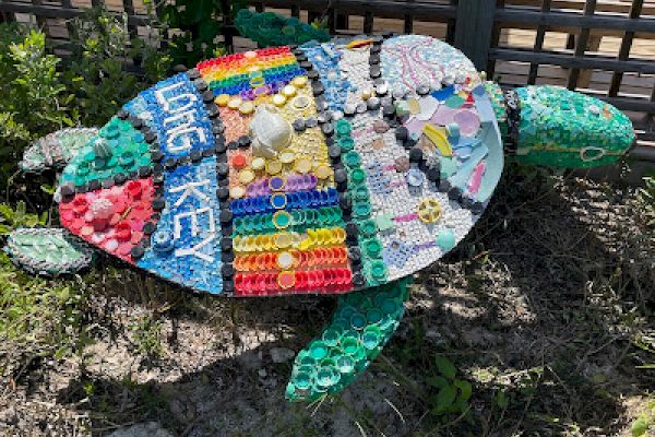 A turtle sculpture made from colorful recycled materials and bottle caps, lying on the ground.