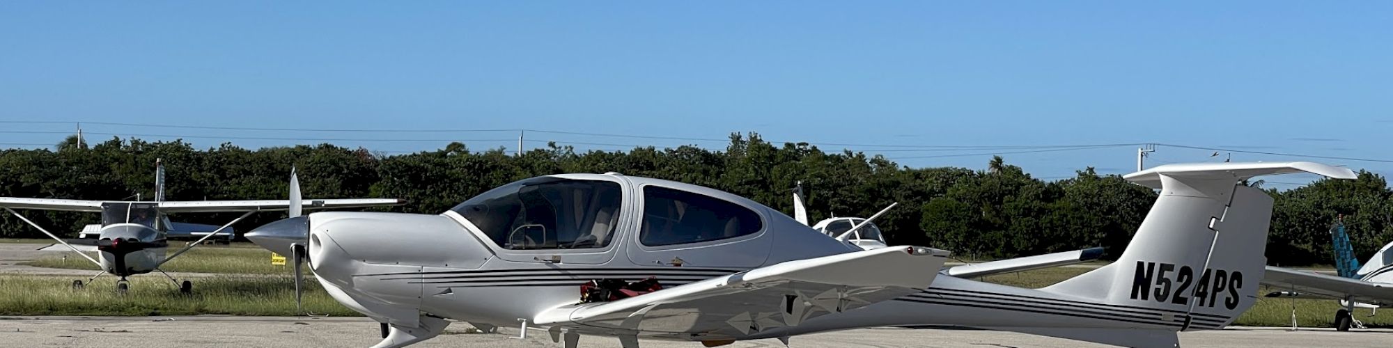 A small aircraft is parked on a tarmac, with orange cones in the foreground and trees in the background.