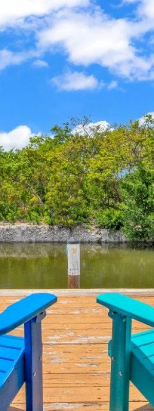 Two colorful chairs overlook a serene canal with lush greenery and blue skies, offering a peaceful and relaxing outdoor setting.